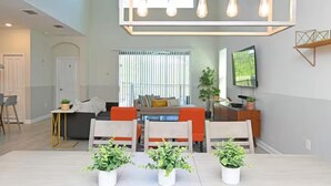 A modern living room with a dining area, a sofa, a TV, and a ceiling light fixture.