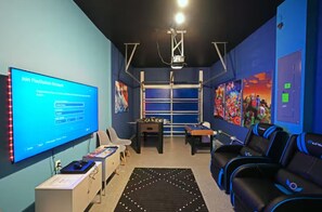 Una habitación con una pantalla grande mostrando una pantalla de inicio de sesión, una mesa de fútbol de mesa, un sofá y un proyector montado en el techo.