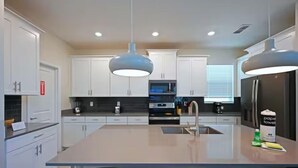 A modern kitchen with white cabinets, a central island, two pendant lights, and a refrigerator.