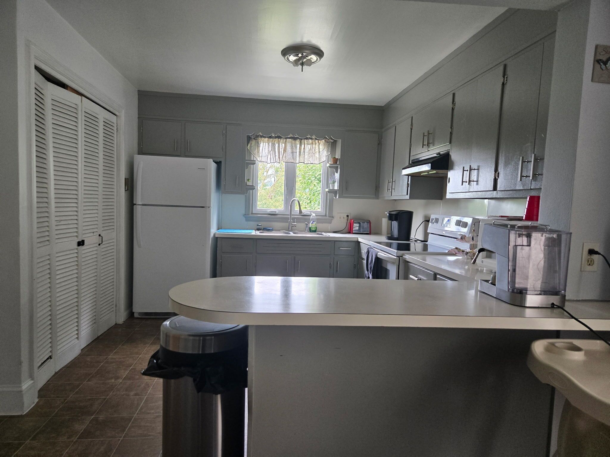 Una cocina compacta con refrigerador, estufa, lavamanos y ventana con vista a follaje.