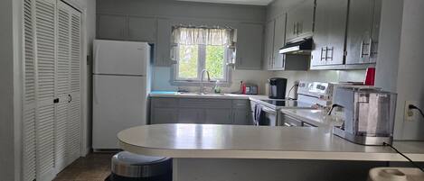Una cocina compacta con refrigerador, estufa, lavamanos y ventana con vista a follaje.