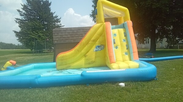 An inflatable water slide with a yellow and orange slide, a blue pool, and a small inflatable house in the background. - Old Farmhouse/Available Horse And Buggy Rides/ Fire pit/ Waterslides (Gap)
