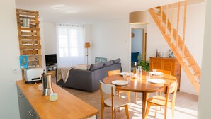 Uma sala de estar moderna com sofá, mesa de jantar e cadeiras, cozinha com bancada de madeira e escada.