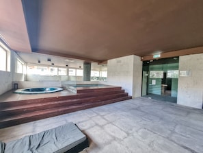 A spacious indoor area with a large hot tub, a small pool, and a staircase leading to a door.