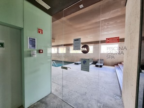 A spa entrance with a glass door, a sign for the Foza Palace Spa, and a pool area visible through the glass.