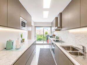 A modern kitchen with a central island, stainless steel appliances, and a view to the outside. - Foz Palace Spa Luxury Residence (Portimão)