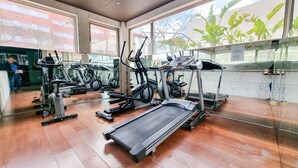 Ein Fitnessraum mit verschiedenen Trainingsgeräten, großen Fenstern und Blick ins Freie.