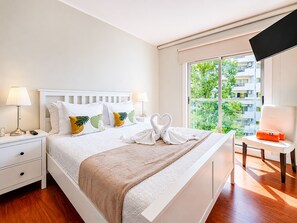 A hotel room with a bed, bedside tables, a TV, a window with a view of buildings, and a chair. - Foz Palace Spa Luxury Residence (Portimão)
