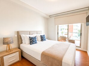 Ein Schlafzimmer mit Bett, Nachttisch, Lampe und Blick durch ein Fenster.