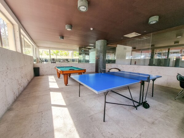 Ein Billardtisch und ein Pooltisch in einem hellen Innenbereich mit großen Fenstern.