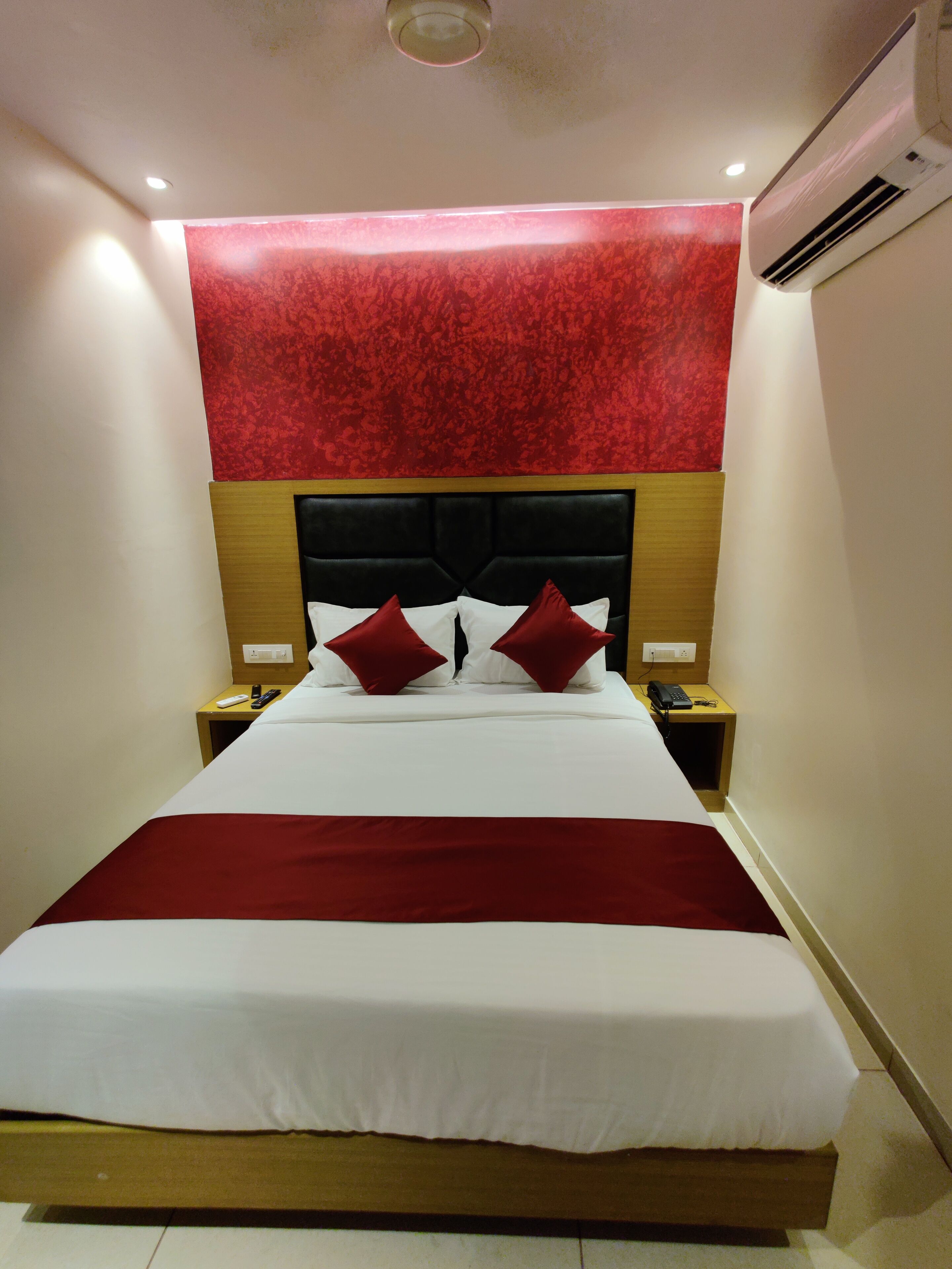 A hotel room with a large bed, a red accent wall, and a wooden headboard.