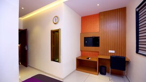 A modern room with a wooden desk, a television, a clock, and a small trash bin. - Hotel Hindustan Residency (Thane)