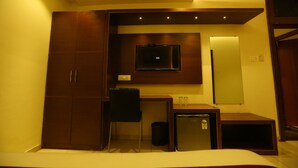 A compact hotel room with a bed, a desk with a chair, a television, and a small cabinet. - Hotel Hindustan Residency (Thane)