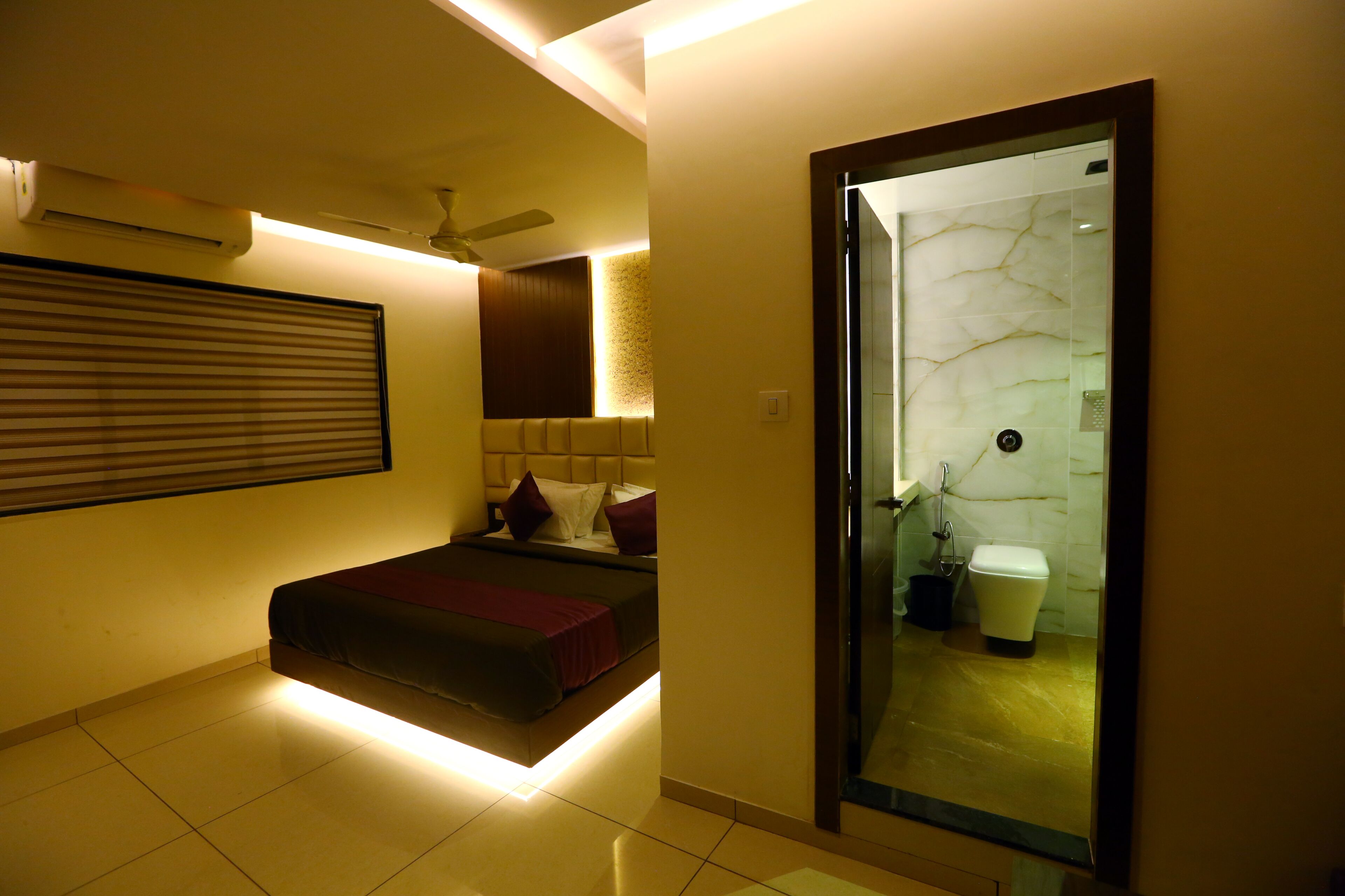 A modern hotel room with a bed, a ceiling fan, a bathroom with a marble wall, and a sliding door.