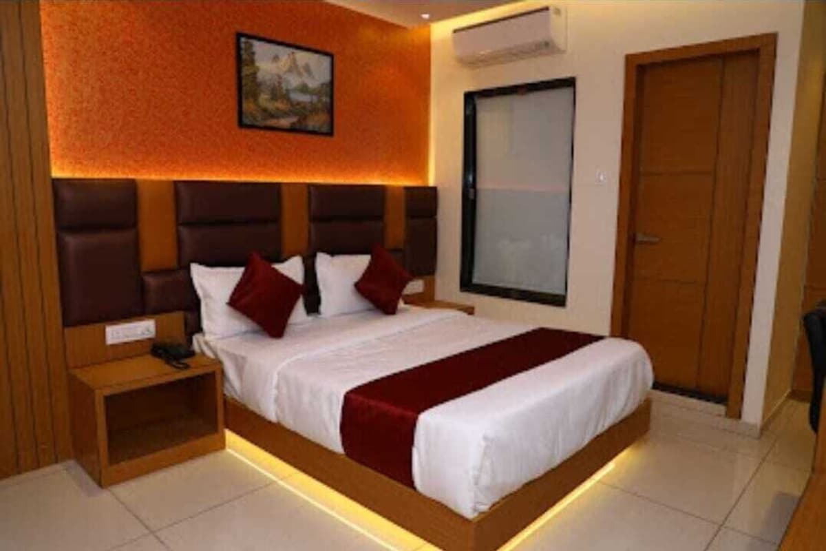 A modern hotel room with a large bed, a bedside table, a wall-mounted air conditioner, and a wooden door.