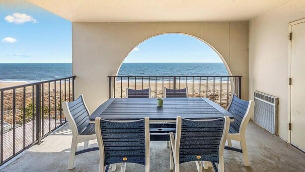 A balcony with a table and chairs, overlooking a beach and the ocean. - Stunning Oceanfront 2 Bedroom With Outdoor Pool! (Ocean City)