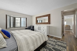 Quarto com cama, cômoda, espelho e janela com persianas.