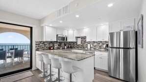 A modern kitchen with white cabinets, stainless steel appliances, and a large island with bar stools. - Stunning Oceanfront 2 Bedroom With Outdoor Pool! (Ocean City)