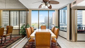 Un espace de repas moderne avec une grande table et des chaises, un ventilateur de plafond et de grandes fenêtres donnant sur la ville.