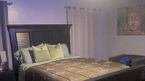 Ein ordentlich bezogenes Bett mit einem gemusterten Überwurf, einem dunklen Kopfteil und einem Nachttisch mit Lampe.