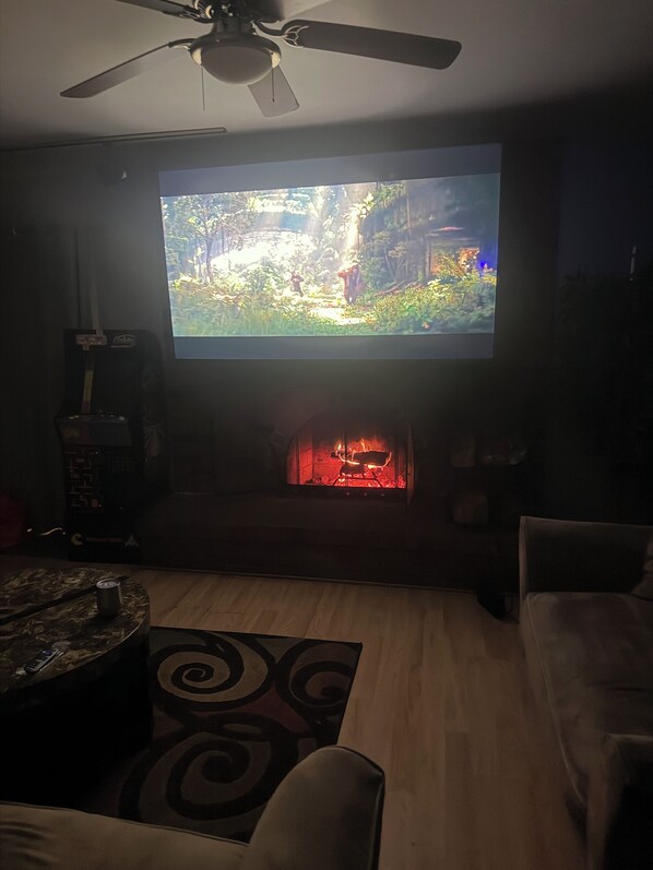 A living room with a flat-screen TV mounted on the wall, a fireplace below it, and a ceiling fan above. - Cozy 4 Bedroom Colonial (Detroit)