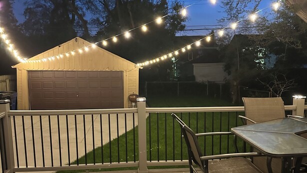 Eine Holzterrasse mit überdachter Sitzgruppe, Lichterketten und einer Garage.