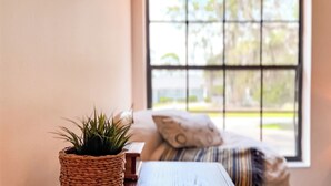 Ein Zimmer mit Fenster, einem gewobenen Blumentopf, einem Holztisch und einem Bett mit gestreifter Decke und Kissen.
