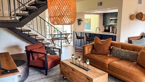 Ein modernes Wohnzimmer mit einem Ledersofa, einem roten Sessel und einem Holztisch. Eine Treppe mit schwarzen Geländern führt zu einer oberen Etage.