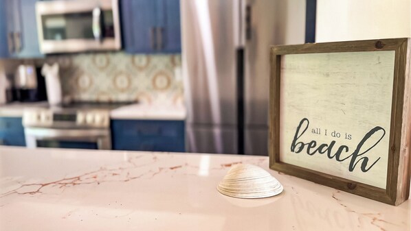 A framed sign with the text "all I do is beach" on a kitchen counter.