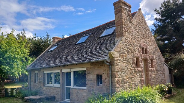 Ein Haus aus Stein mit geneigtem Dach, Oberlichtern und einer kleinen Veranda.