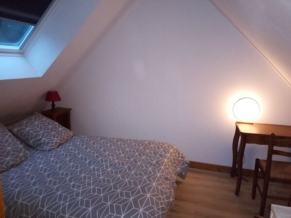 Une chambre avec un plafond en pente, un lit avec une literie à motifs, une table de chevet avec une lampe et un bureau avec une chaise.