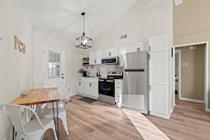 Una cocina moderna con armarios blancos, electrodomésticos de acero inoxidable y una mesa de comedor de madera con sillas.