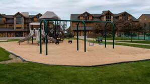 Ein Spielplatz mit Rutschen und Schaukeln, umgeben von Sand und Rasen.