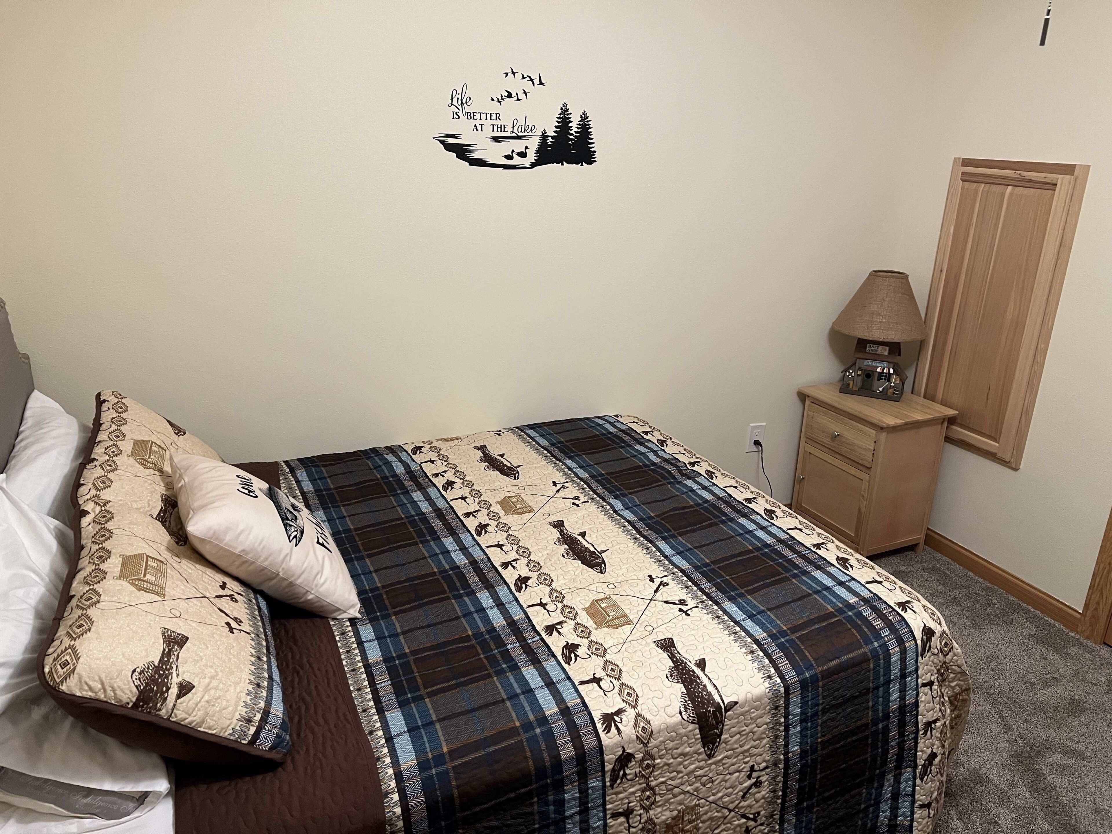 A bedroom with a bed, pillows, a wall decal, a nightstand, and a wooden wardrobe.