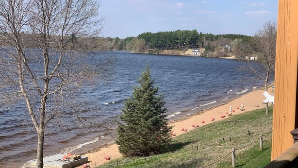 Blick auf ein Seeufer mit einer Holzterrasse, einem Sandstrand und einer Reihe roter Trainingsbälle.