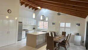 A modern kitchen with white cabinets, a central island, and a dining area with a table and chairs. - Ashmore - Four bedroom home, easy walk to shops and beach, back deck with a view (South West Rocks)