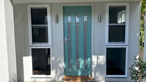 A house with a teal front door, white siding, and three windows. - Ashmore - Four bedroom home, easy walk to shops and beach, back deck with a view (South West Rocks)
