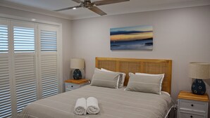 A bedroom with a bed, two bedside tables, a ceiling fan, and a painting on the wall. - Ashmore - Four bedroom home, easy walk to shops and beach, back deck with a view (South West Rocks)