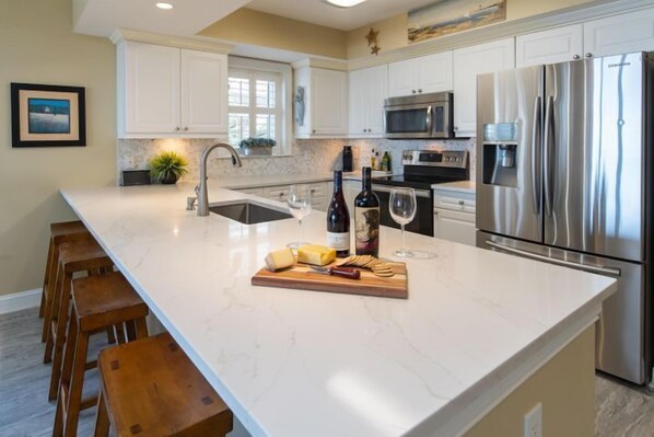 A modern kitchen with white cabinets, stainless steel appliances, and a marble countertop.