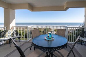 A round table with chairs on a balcony overlooking the ocean.