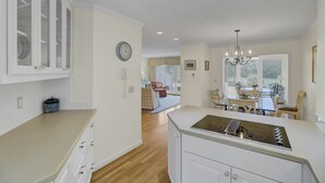 A modern kitchen with white cabinetry, a built-in stove, and a dining area with a chandelier. - 43 Fairway Dunes by AvantStay | Coastal Charm + Golf! (Isle Of Palms)