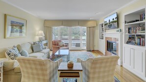 A living room with a sofa, armchairs, a coffee table, a fireplace, and a bookshelf. - 43 Fairway Dunes by AvantStay | Coastal Charm + Golf! (Isle Of Palms)