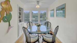 A dining area with a glass table and metal chairs, large windows with a view of greenery, and a ceiling fan. - 43 Fairway Dunes by AvantStay | Coastal Charm + Golf! (Isle Of Palms)