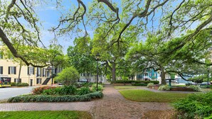 A brick pathway lined with trees and shrubs, leading to a row of buildings with a mix of architectural styles.