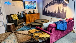Ein Wohnzimmer mit modernem Design, ausgestattet mit einem pinken Sofa, einem Holztisch, einem an der Wand montierten Fernseher und einem großen Gemälde einer Berglandschaft.