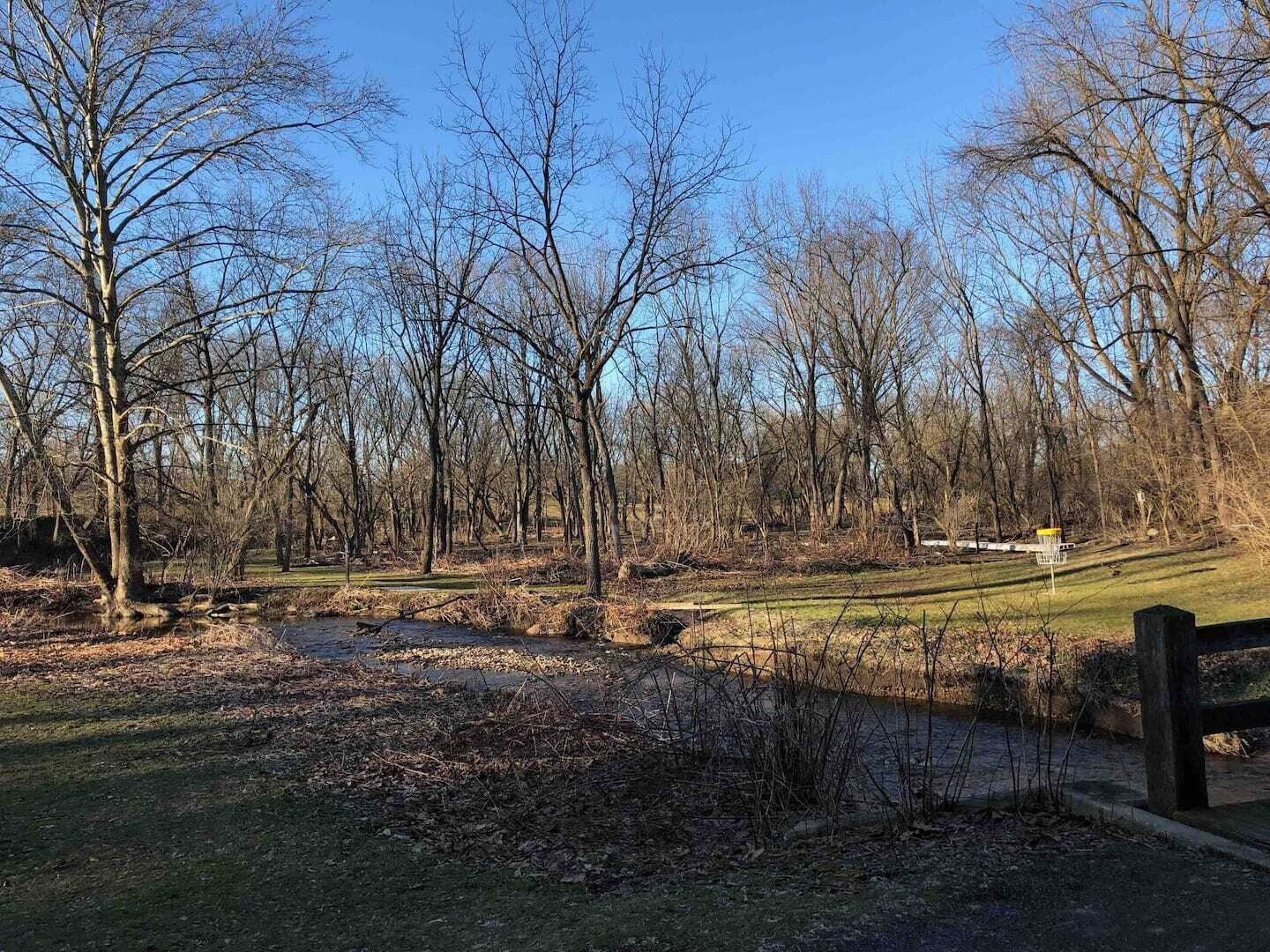 A park with a golf course, trees, and a wooden fence.