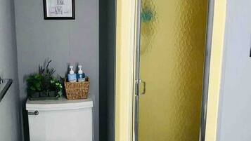 A bathroom with a toilet, a shower with a glass door, a framed certificate on the wall, and a basket with toiletries.