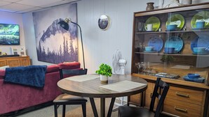 Ein gemütlicher Essbereich mit einem runden Holztisch, zwei Stühlen, einem kleinen Topfpflanzen und einer Vitrine mit Glasüren, in der Geschirr ausgestellt ist.