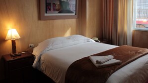 A hotel room with a bed, a nightstand with a lamp, a framed artwork on the wall, and a window with curtains. - KAARO HOTEL SUITE (Puno)