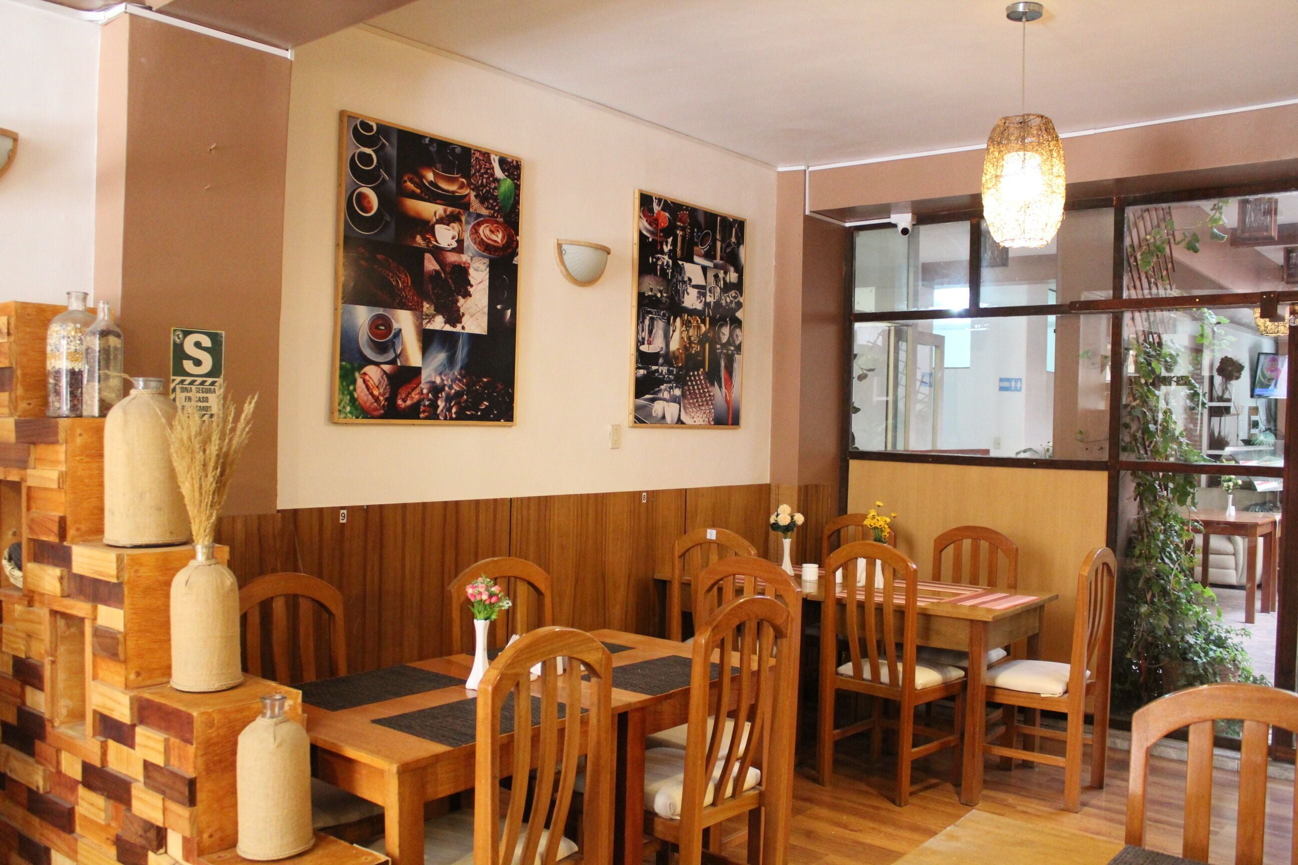 Interior de restaurante con mesas y sillas de madera, un panel de menú en la pared y un ventanal con vistas al exterior.
